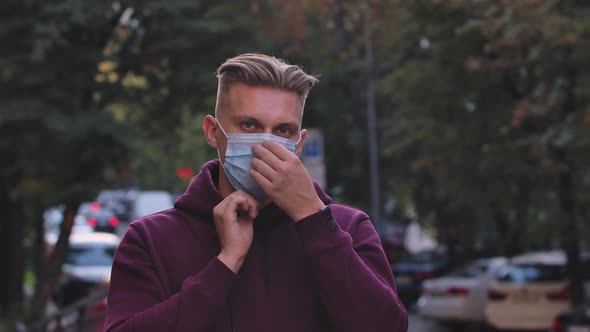 Portrait of Young Man Looking at the Camera and Putting Medical Mask on Face for Protection Against