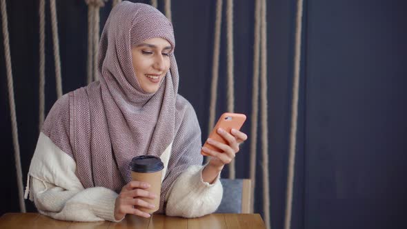 Adult Cheerful Muslim Woman Is Reading Sms in Mobile Phone and Smiling in Cafe