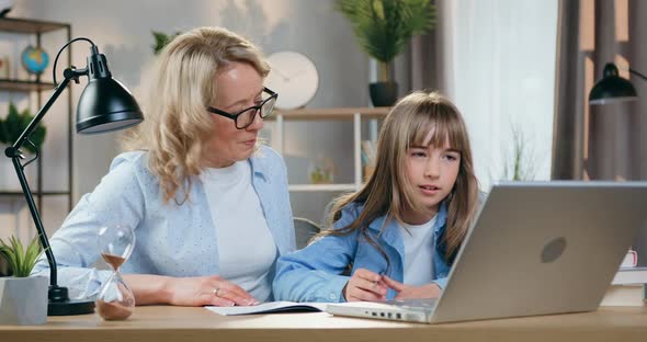 Mother in Glasses Helping Her Smart Daughter with Homework, Sitting at Workplace