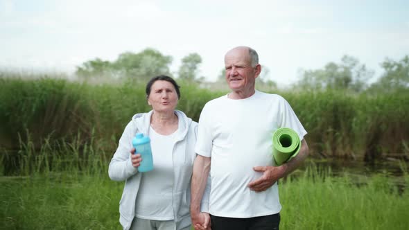 Cheerful Old Man and Woman Take Care of Their Health Go Holding Hands After a Morning Workout