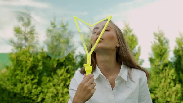 Young Beautiful Woman Makes Soap Bubbles in Summer on a Sunny Day Against the Background of Green