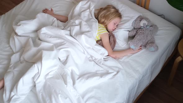 Blonde Little Girl Sleeping in Big Bed with White Bedding
