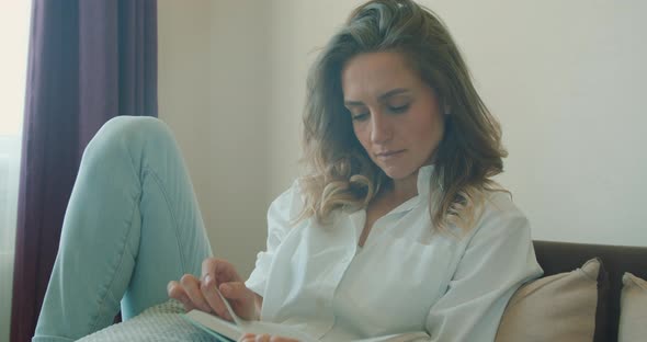 Front View Close Up of a Young Woman Sitting on a Sofa Reading a Book at Home, Social Distancing.