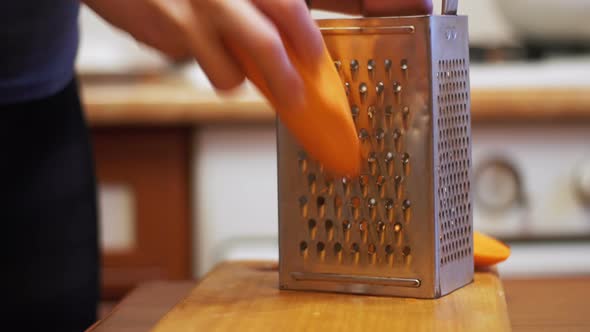 Woman Hands Rubbing Carrots on Grater in a Home Kitchen