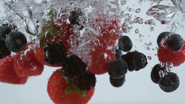 Slow motion shot of raspberries, strawberries and blueberries splashing into water, shot with Phanto