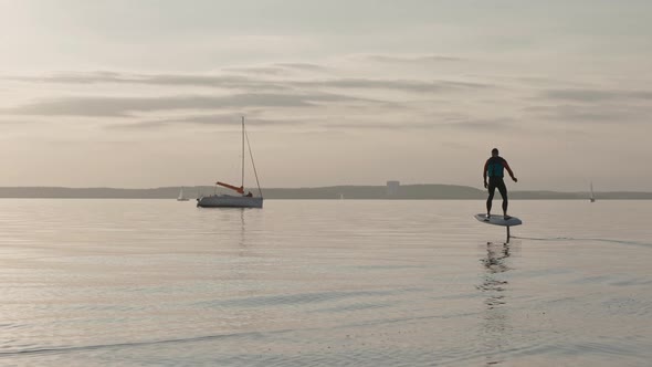 Man Riding on a Hydrofoil Surfboard on Large Lake at Golden Sunset