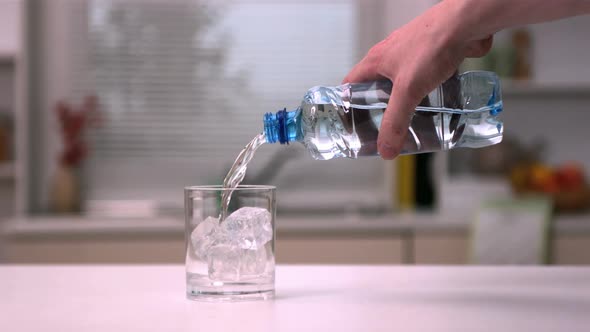 Hand pouring water into a glass with ice cubes