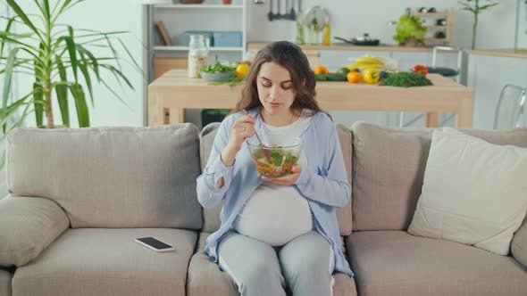 Pregnant Woman With Great Pleasure Eating Vegetable Salad on the Couch