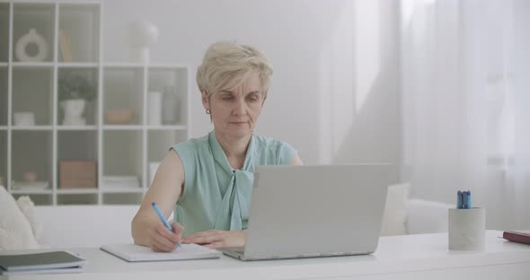 Middle-aged Woman Is Working with Laptop, Viewing Webinar and Writing Notes, Distant Self-education