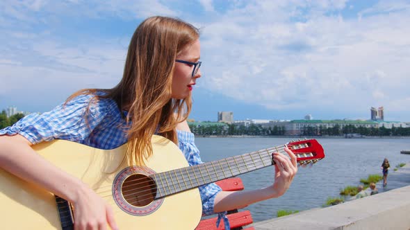 A Woman is Playing the Acoustic Guitar Outdoors