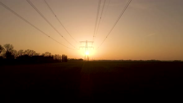 Low angle dolly under powerlines and high voltage tower during sunset