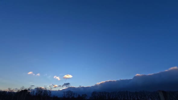 Time lapse dark clouds obscure the evening sun at sunset, and clear blue skies.