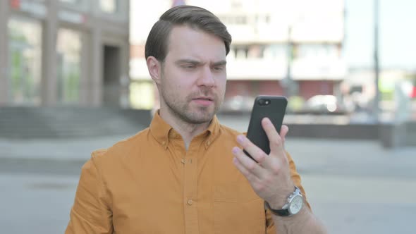 Upset Young Man Reacting to Loss on Smartphone Outdoor