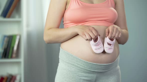 Pregnant Woman Expecting Baby, Playing With Infant Shoes on Big Belly, Happiness