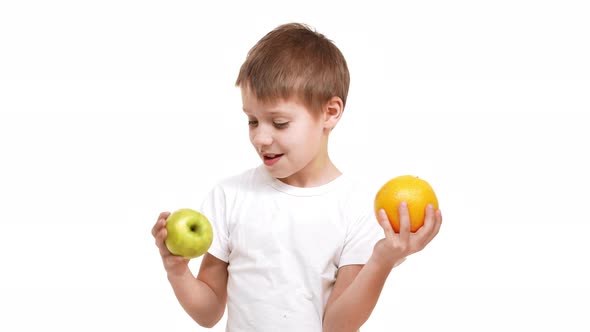 Young Smiling Caucasian Boy Holding Big Apple and Orange in Hands Exploring Them Smelling and