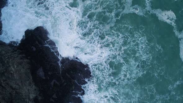 Aerial of waves crashing against UK coast, rising top down view