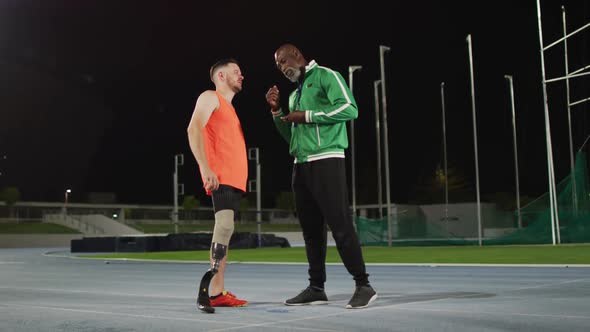 Diverse male coach and disabled male athlete with running blade standing and talking