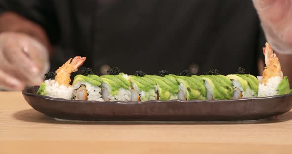 Chef Putting Black Caviar (roe) On Top Of Avocado On The Sushi Rolls. - close up shot