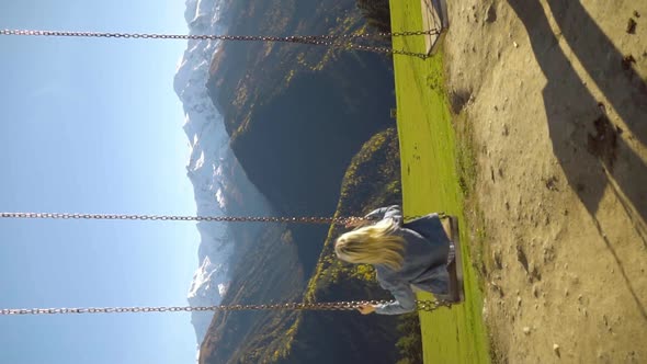 woman rides on large swing against background of mountains in Georgia,