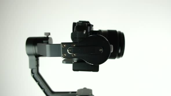 Gimbal with digital camera rotates on white background.