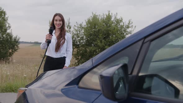 Smiling Girl Holds the Charger of Her Electric Car