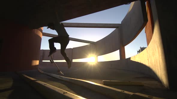 Silhouette of a young man skateboarding down a spiral ramp in a parking garage at sunset.