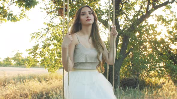 young happy woman swaying rope swing on oak tree,summer leisure at sunset, healthy lifestyle