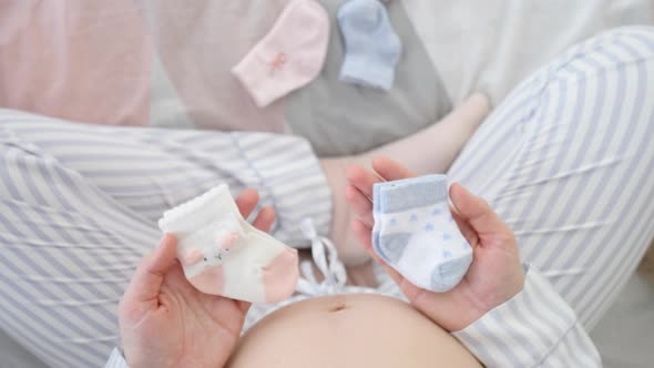 Pregnant Woman Holding Baby Socks For A Boy And A Girl