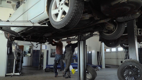 The car goes down on the lift and two mechanics repair suspension car