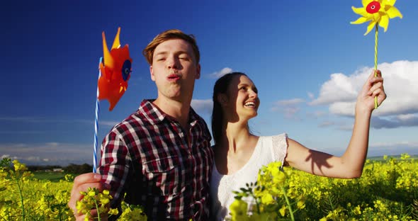 Romantic couple blowing pinwheel in mustard field