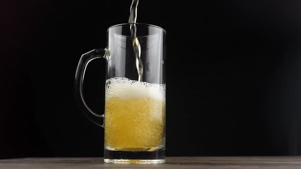 Beer is pouring and foaming in Glass on black background closeup