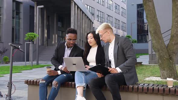 Smiling Hardworking Multiethnic Young Colleagues which Working with Computer Outdoors