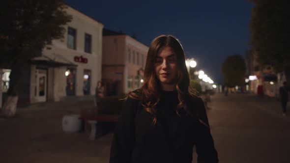 A Beautiful Young Girl Stopped on the Background of a Row of Burning Street Lamps and Crosses His