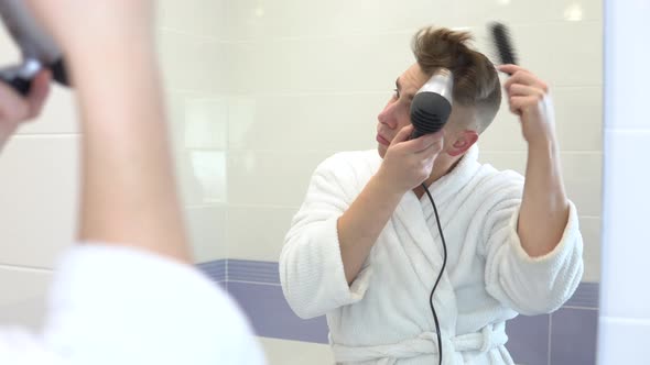 A Young Man Dries His Hair with a Hairdryer. A Man in a White Coat Makes Styling Using a Hairdryer