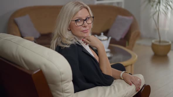 Expert Caucasian Female Psychologist Sitting on Comfortable Armchair in Office Looking at Camera