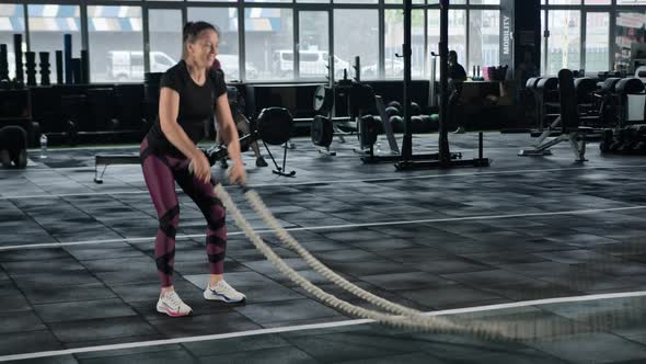 Young female athlete trains in the gym with ropes, crossfit, endurance training