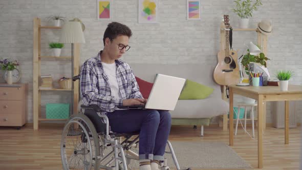 Portrait Young Asian Man in Stylish Glasses Disabled in a Wheelchair with a Laptop in the Living