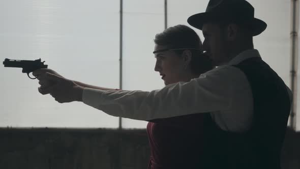 Portrait Elegant Young Woman in Red Dress Aiming a Gun, Handsome Gallant Man Stands Behind