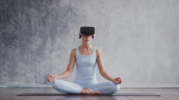 Young and sporty girl in sportswear is doing exercises at home using virtual reality helmet.