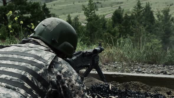 View from over the shoulder of a soldier as he is shooting a belt-fed machine gun alt