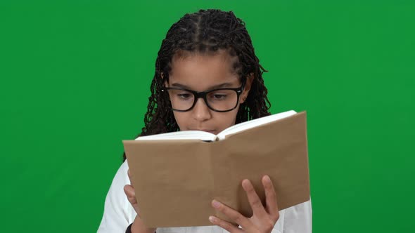Charming African American Teen Girl in Eyeglasses Reading Book on Green Screen Looking at Camera