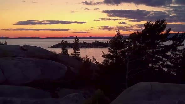 Fly Past Inukshuk on Rocky Pine Tree Island just after Sunset, Drone Aerial Wide Dolly In. Colorful