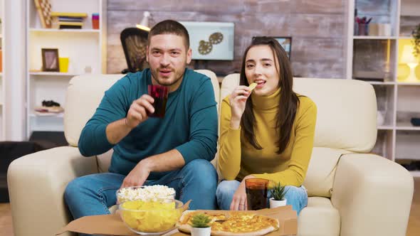 Couple Sitting on Couch Laughing While Watching Tv and Eating Pizza