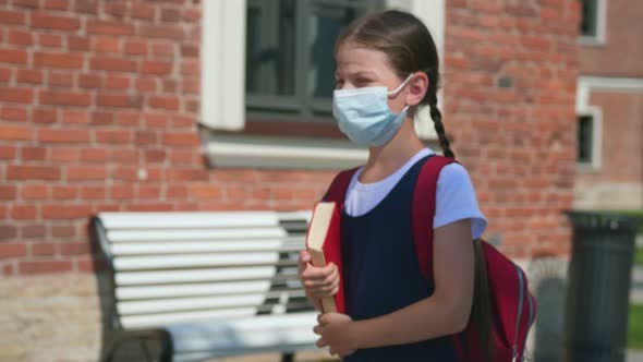Side View of Preteen Girl with Medical Mask and Book Walk to School