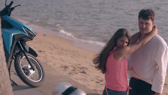 Girl Hugs Handsome Tall Man on Beach Against Blue Ocean