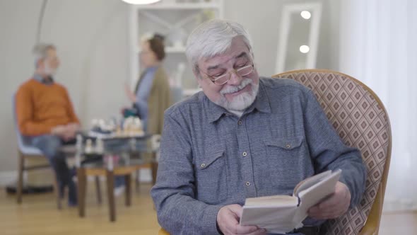 Portrait of Mature Caucasian Man in Eyeglasses Reading Book in Nursing Home. Elderly Male Retiree