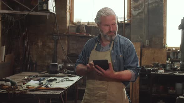 Blacksmith Working on Digital Tablet in Smithy