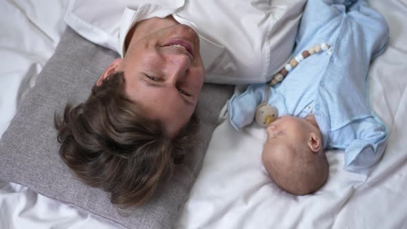 Top View Young Father Admiring Newborn Son Lying on White Bed and Looking at Camera Smiling