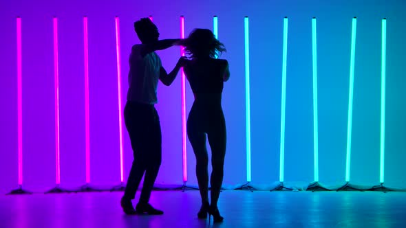 Professional Dancers Dancing Salsa in the Studio Against the Backdrop of Multicolored Neon Lights in