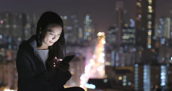 Woman using mobile phone over city background at night